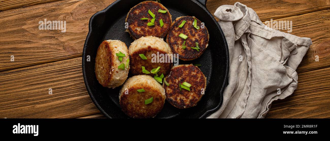 Cotolette fatte in casa di pesce, pollo o carne su una padella in ghisa nera padella padella padella su un tavolo di legno rustico, tradizionale pasto arrosto salubre cotolette in Foto Stock