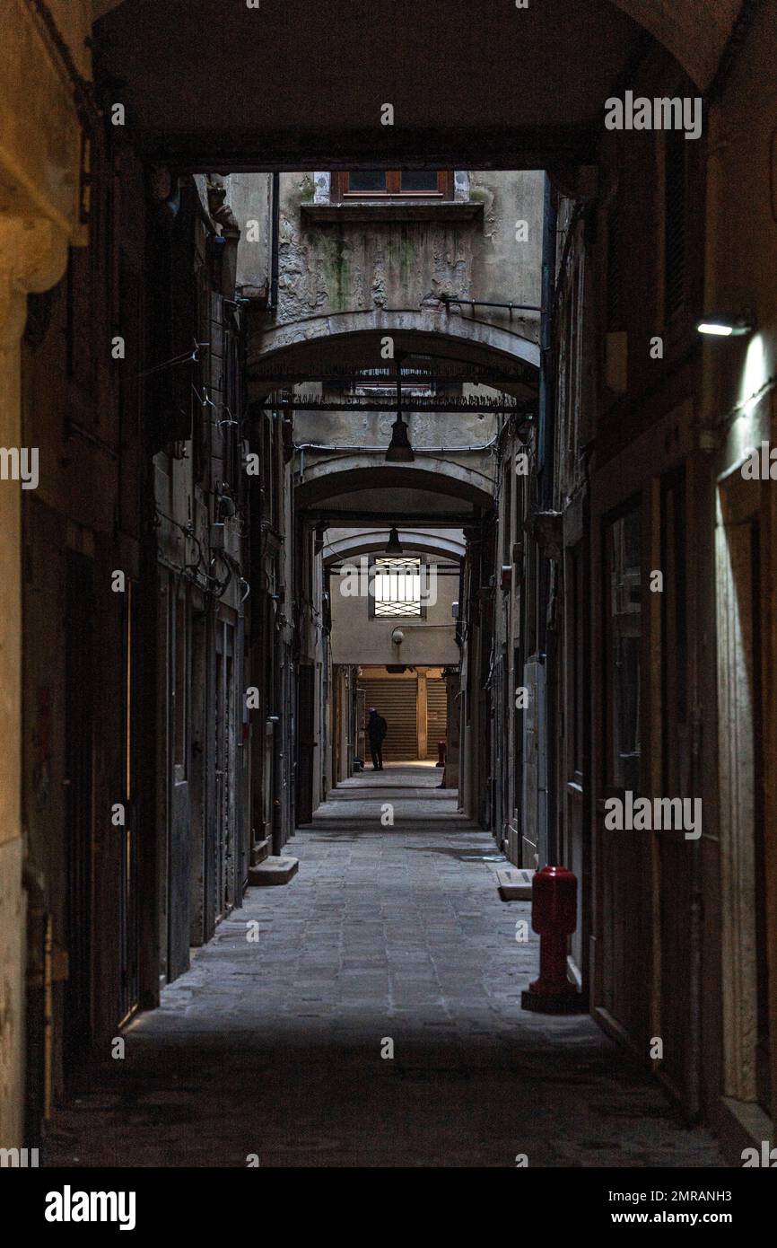 Un vicolo vuoto e scuro con una figura sola in lontananza nella città di Venezia. Foto Stock