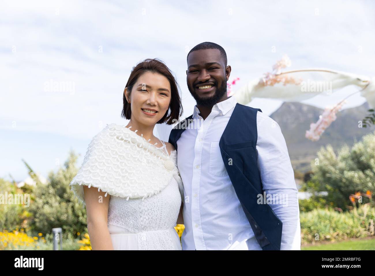 Ritratto di sposa felice e variegata sorridendo alla fotocamera durante il matrimonio all'aperto Foto Stock