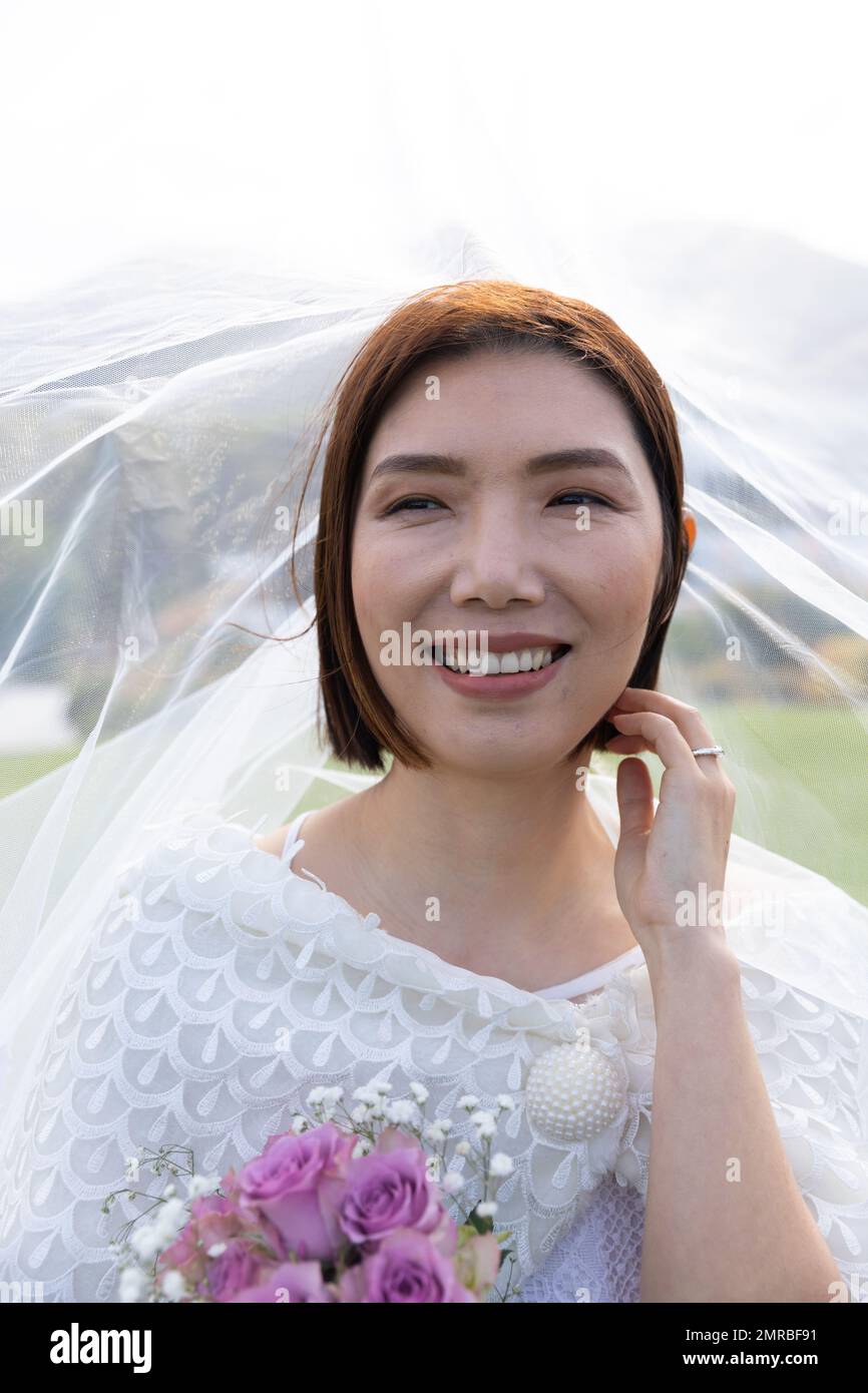 Ritratto verticale di sposa asiatica sorridente che indossa il velo alle nozze all'aperto, spazio copia Foto Stock