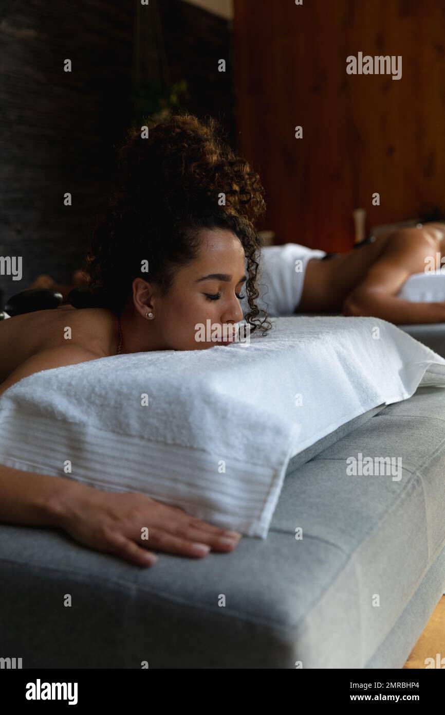 Verticale della donna biracial distesa sul tavolo di massaggio che ha il trattamento delle pietre calde alla stazione termale, spazio della copia Foto Stock