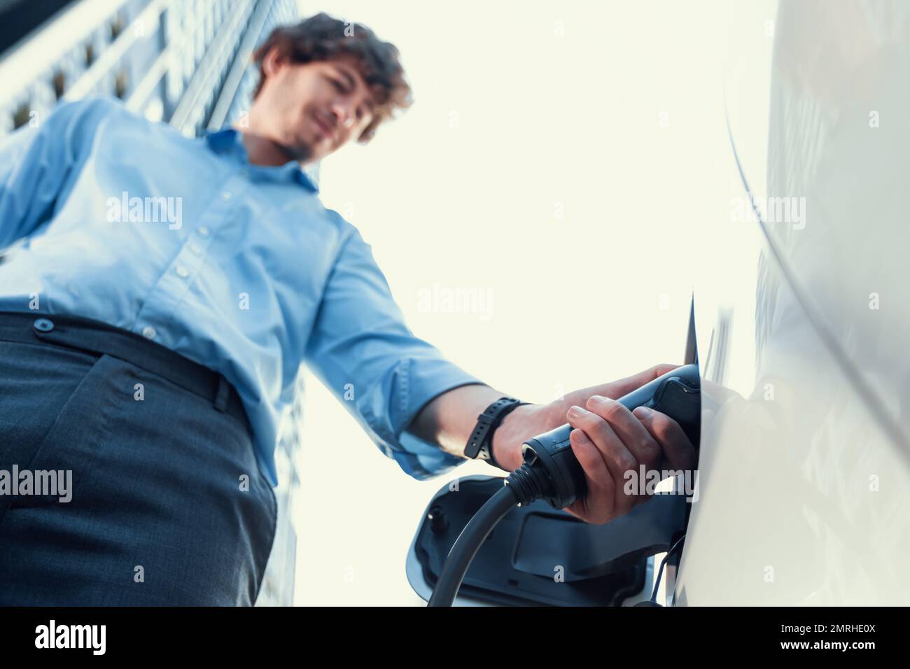 Fisheye vista mettere a fuoco sulla mano inserire il caricabatterie EV spina in auto elettrica con sfondo sfocato di progressive città moderno stile di vita-uomo d'affari ricaricare la sua Foto Stock