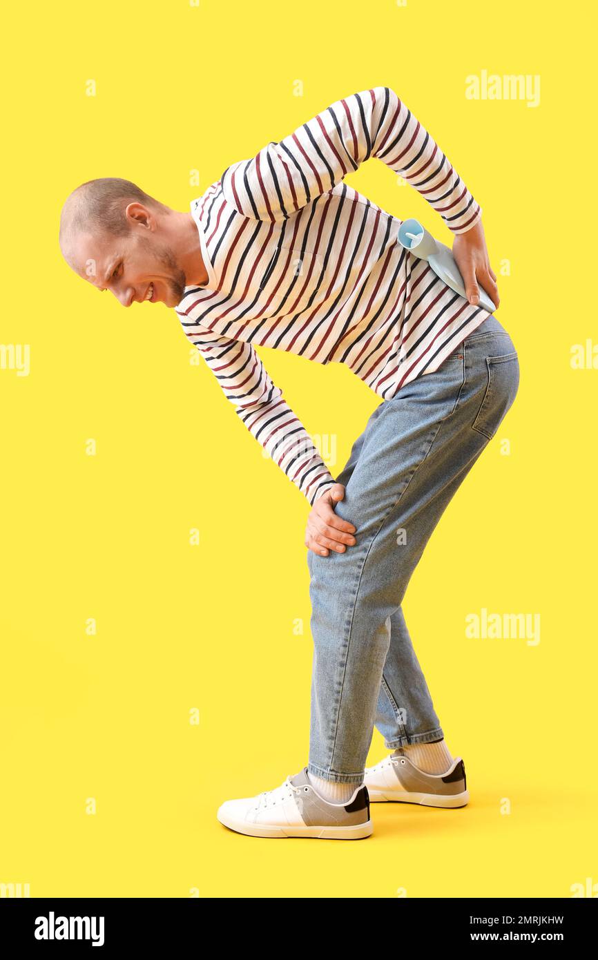 Giovane uomo che scalda la parte inferiore della schiena con una bottiglia  d'acqua calda su sfondo giallo Foto stock - Alamy