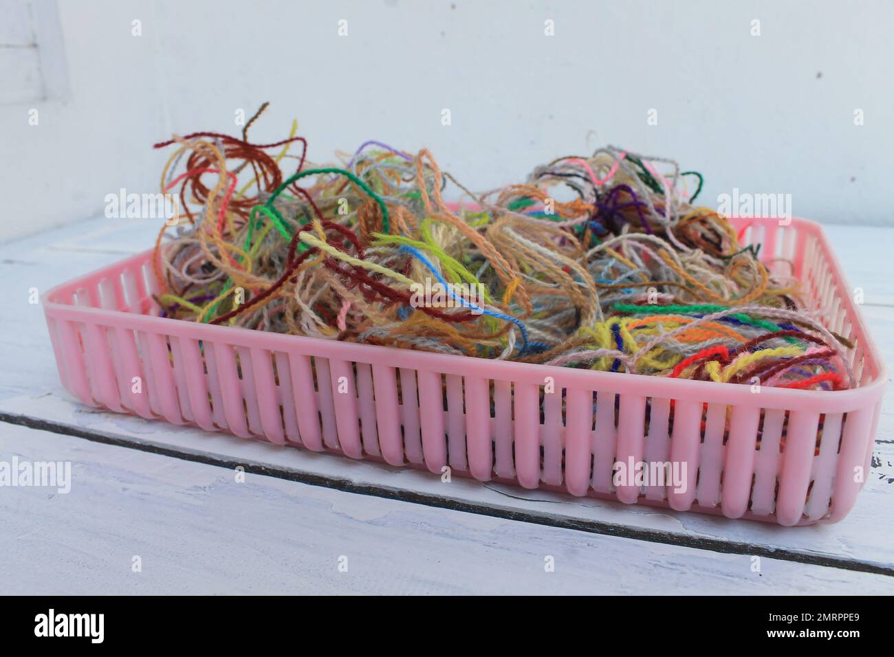 Un mazzo di filo di lana colorato rimasto in un contenitore di plastica rosa sul tavolo Foto Stock