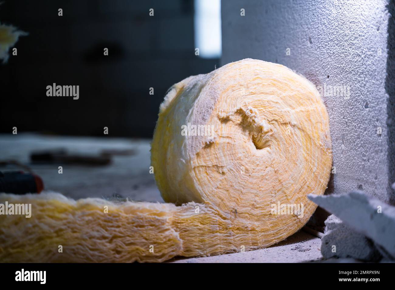 Un rotolo di isolamento in lana di vetro da vicino in un cantiere con sfondo sfocato. Materiale universale di conforto e isolamento in pallido Foto Stock