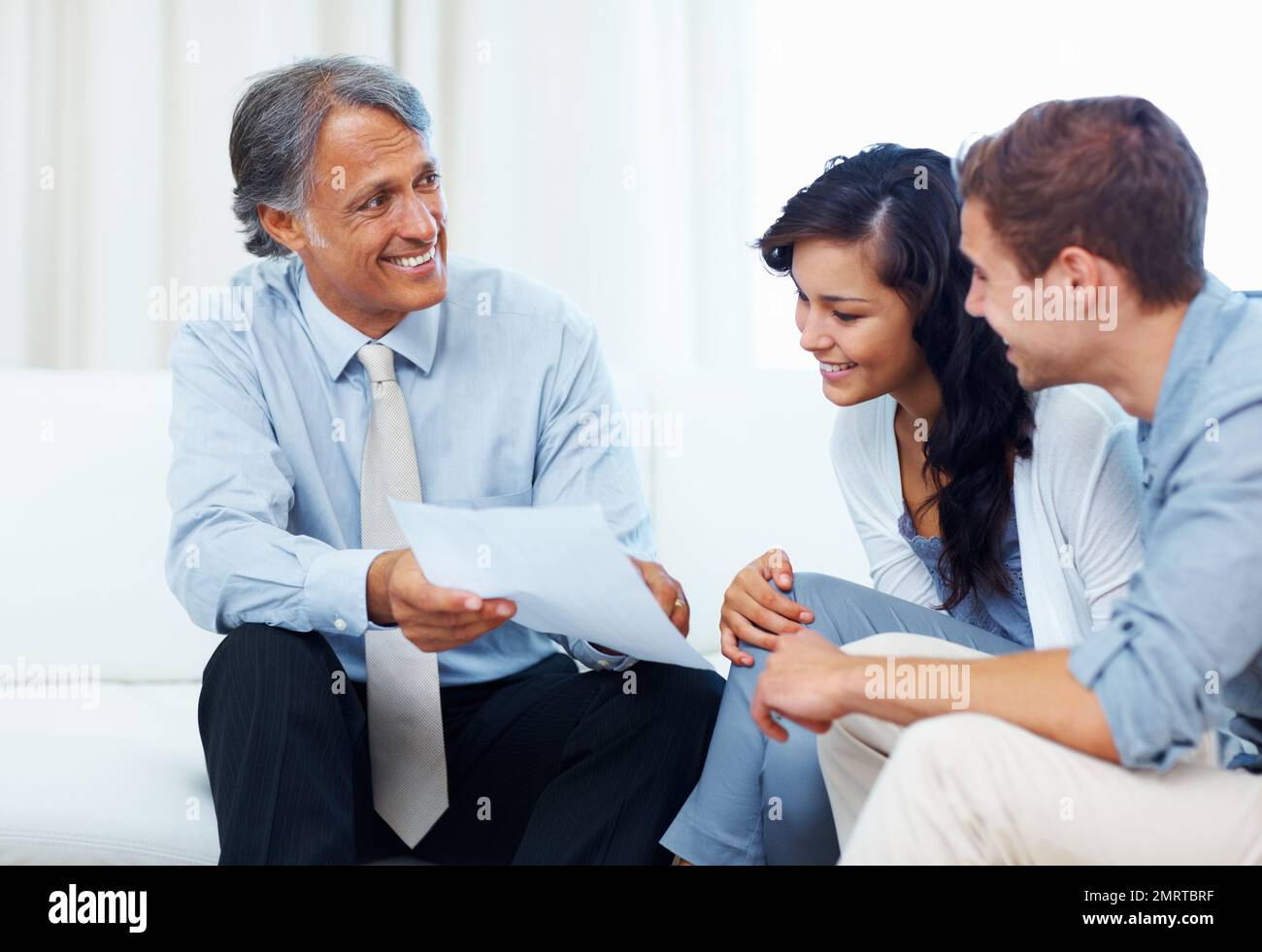 Coppia che discute con pianificatore finanziario. Consulente maturo che mostra il piano finanziario a una giovane coppia a casa. Foto Stock