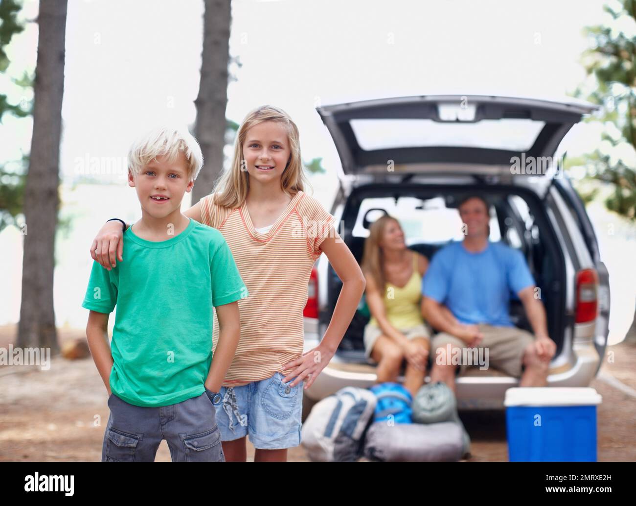 Giovani fratelli che si godono la vacanza. Ritratto di giovani fratelli in piedi all'aperto con i genitori seduti in macchina. Foto Stock