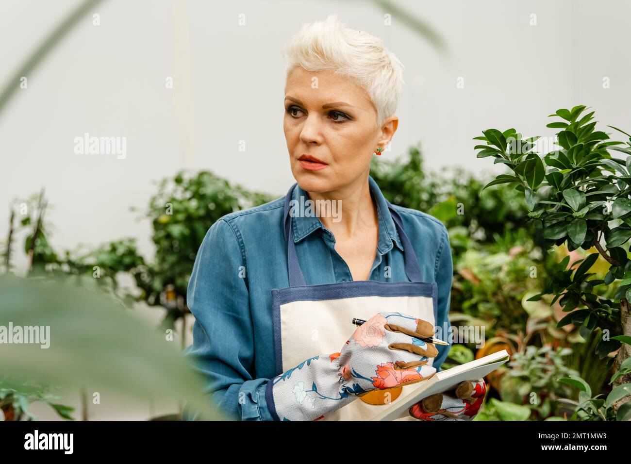 Donna serio giardiniere che controlla le piante, prendendo appunti sul verde. Foto Stock