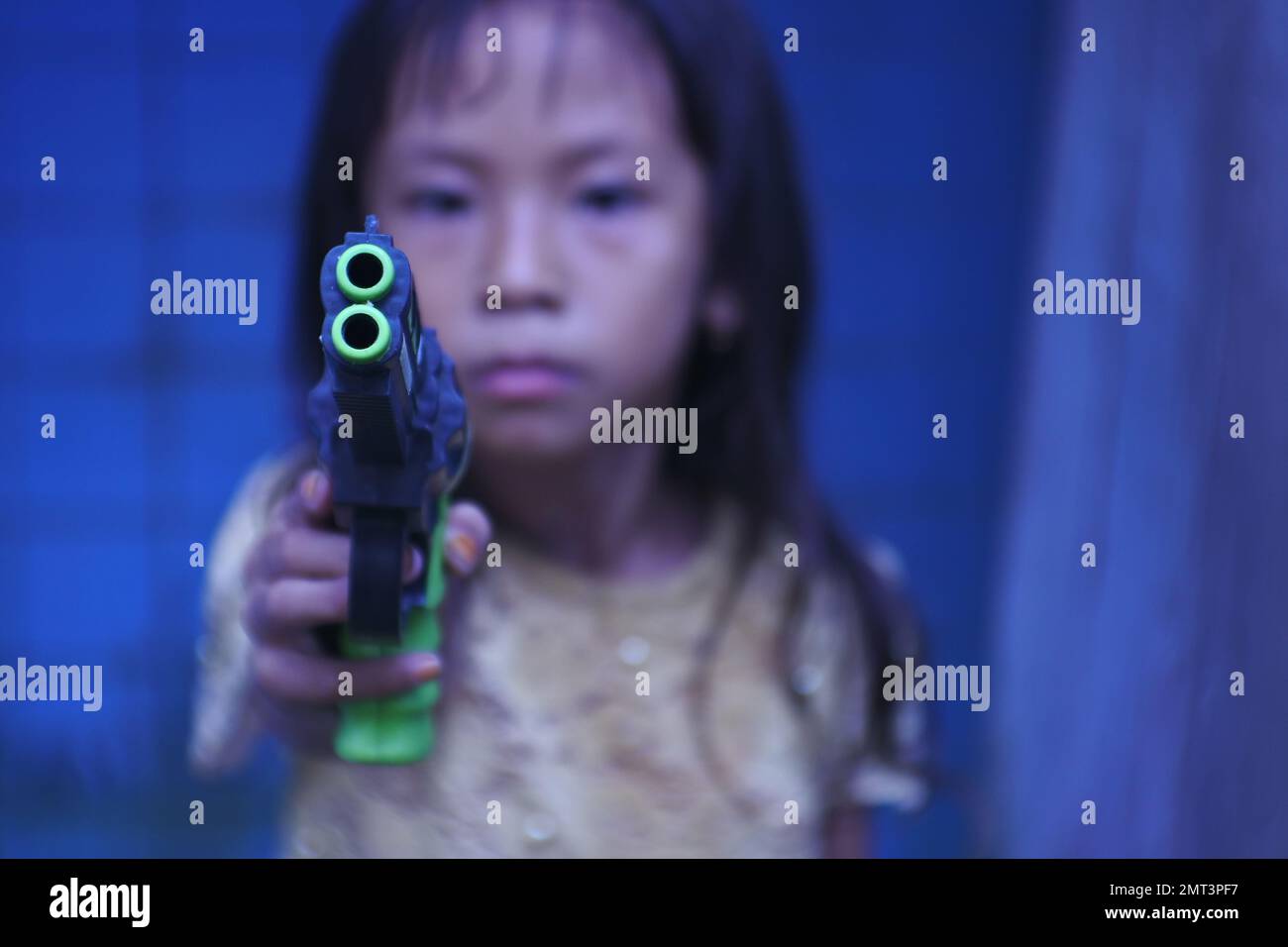 Una ragazza triste che punta una pistola giocattolo sulla fotocamera in una messa a fuoco selettiva Foto Stock