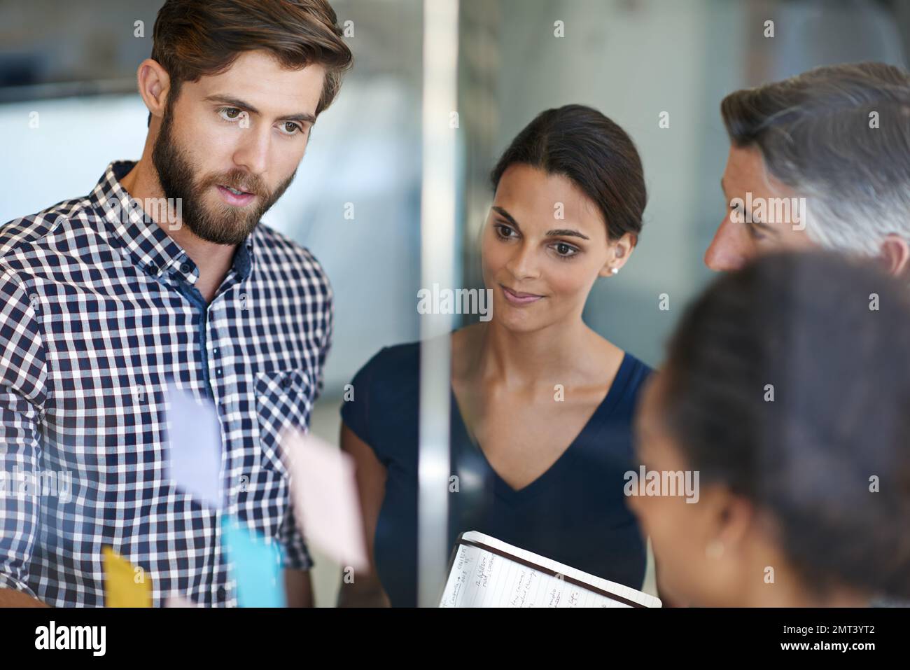 Decidere il modo migliore per andare avanti... i colleghi organizzano appunti appiccicosi su una parete di vetro durante una sessione di brainstorming. Foto Stock