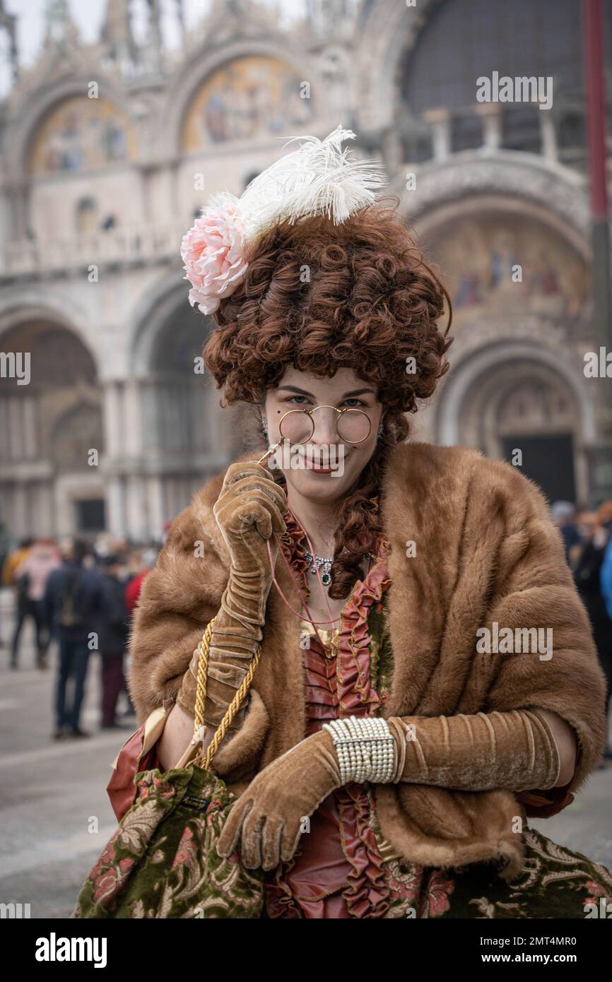 Elegante giovane donna vestita di vestito da opera-vestito, guanti e stile XIX vestito con una parrucca sulla testa e lorgnette in mano che sta guardando attraverso co Foto Stock