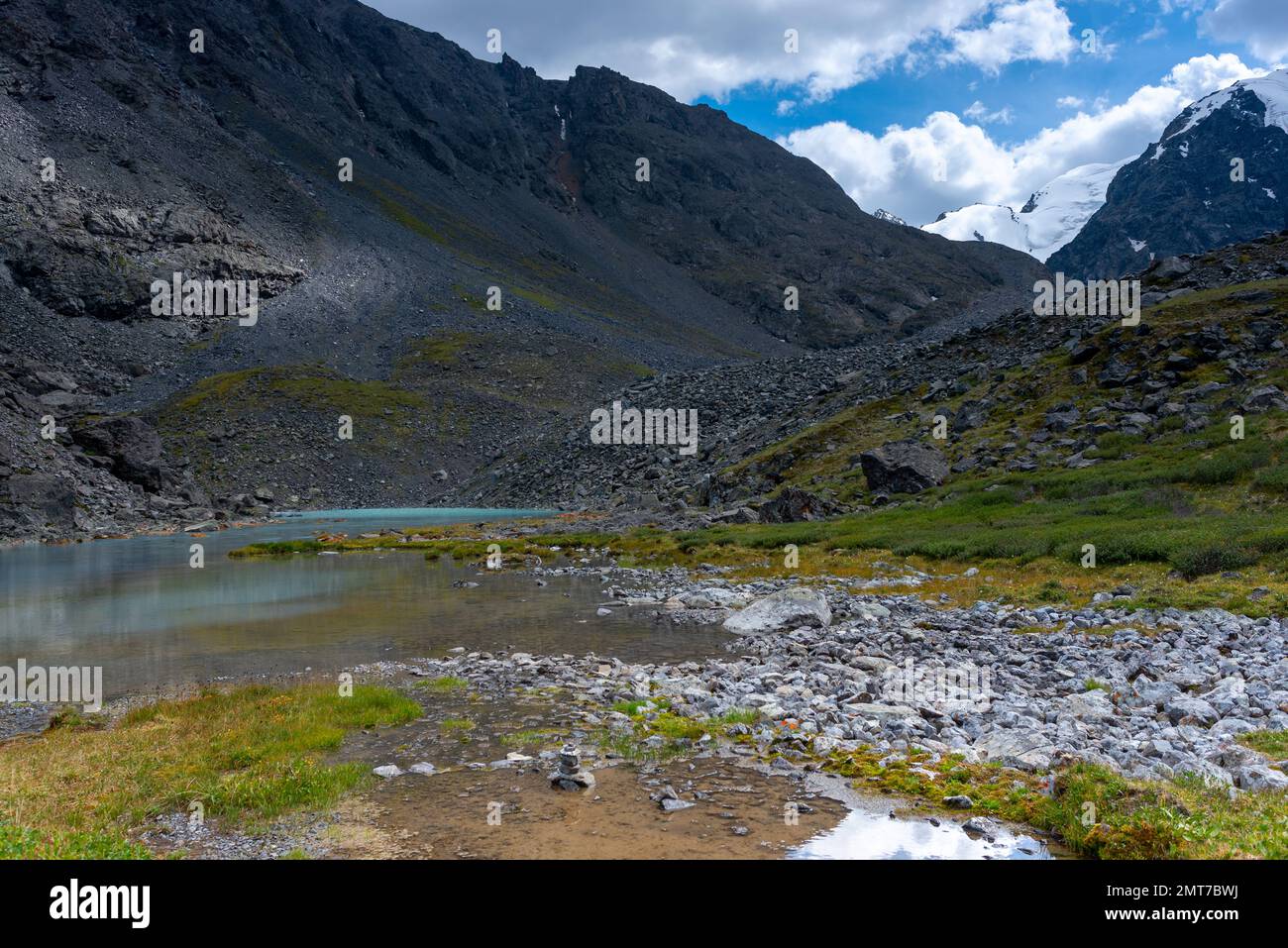Lago di montagna con acqua limpida Karakabak nelle montagne Altai con cime innevate e ghiacciai con sotto le nuvole e erba verde. Foto Stock
