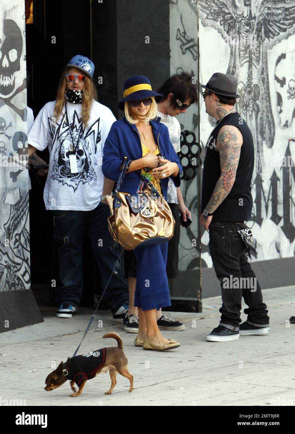 Una di queste cose non è come le altre! Paris Hilton, con il suo piccolo cane al traino, sembra un po' fuori posto con il suo abito colorato e il grande cappello blu mentre lei e il ragazzo Benji Madden fanno una sosta per fare shopping al negozio Benji, il DCMA Collective. Hollywood, California. 5/20/08. Foto Stock