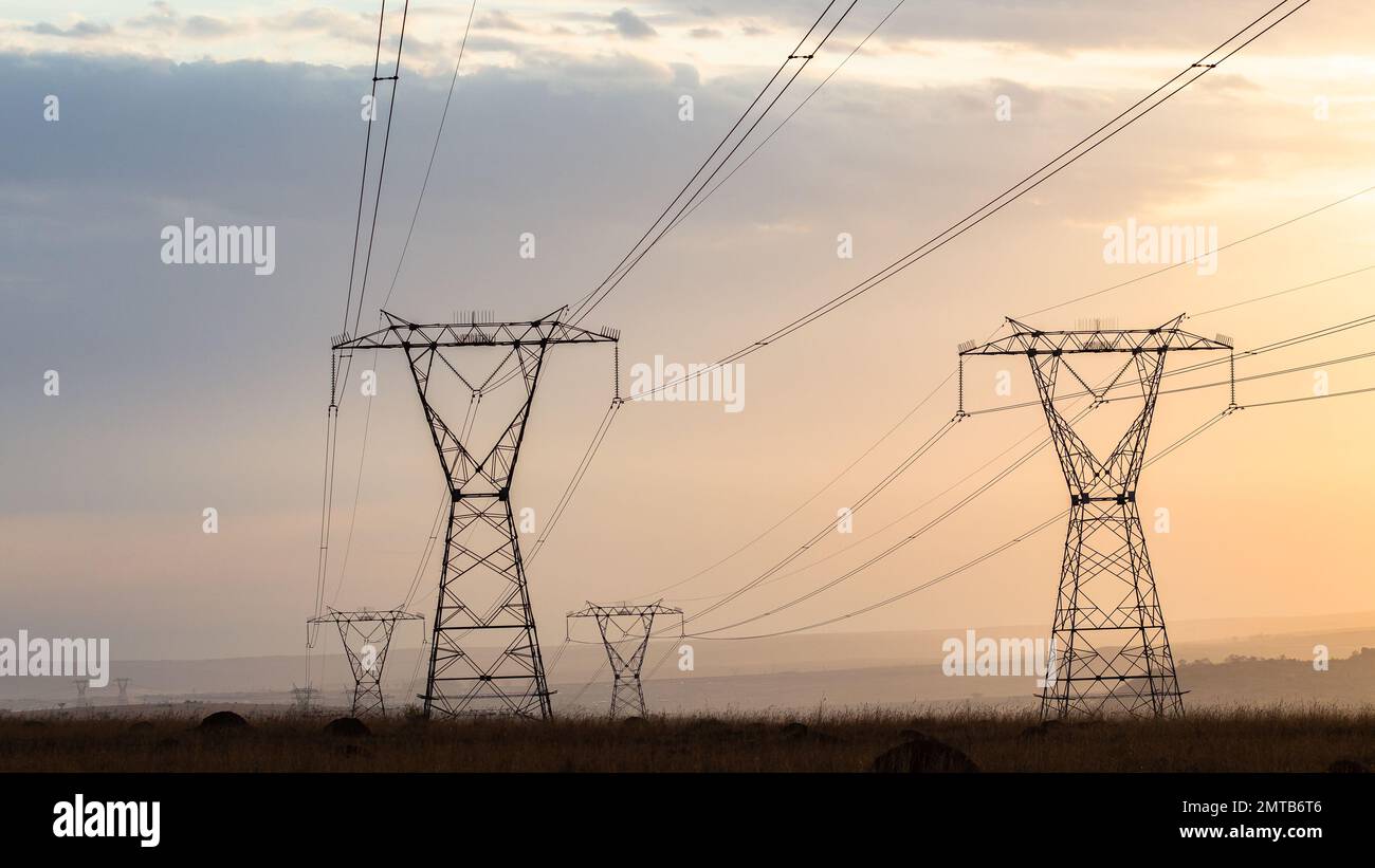 Le strutture di linea elettrica che trasportano energia elettrica contrastano durante la luce del crepuscolo mattutino nella campagna. Foto Stock