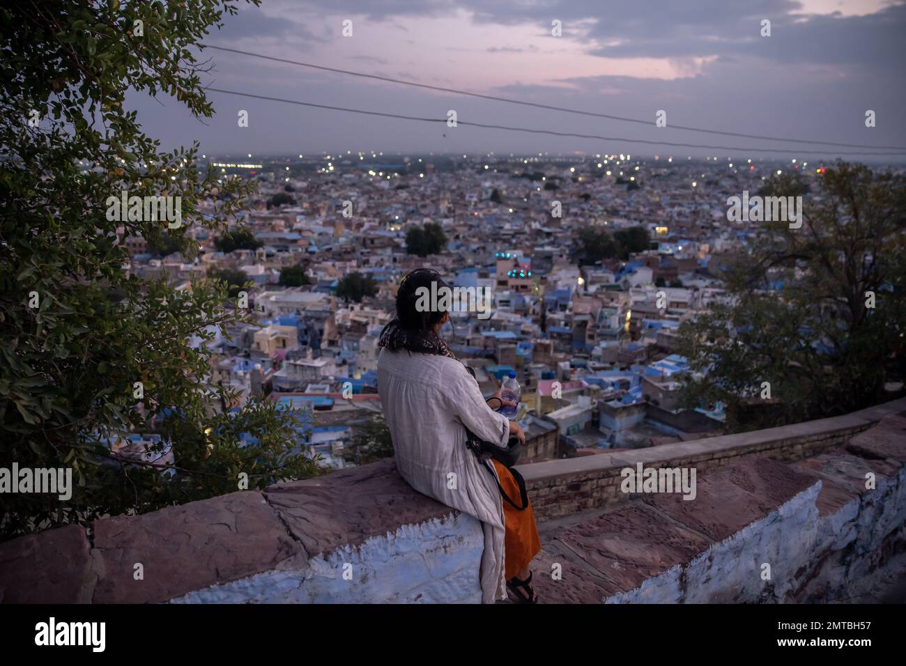 Una ragazza seduta su una parete che guarda una vista di Jodhpur sullo sfondo. Jodhpur, Rajasthan, India. Foto Stock