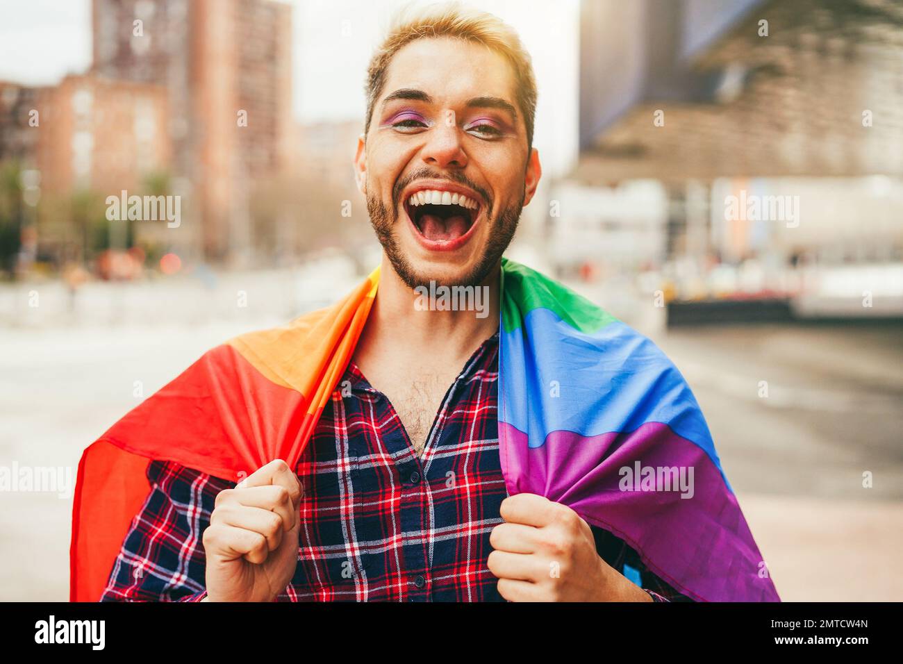 Gay uomo con trucco su divertirsi indossando lgbt arcobaleno bandiera all'aperto - Focus principale sulla bocca Foto Stock