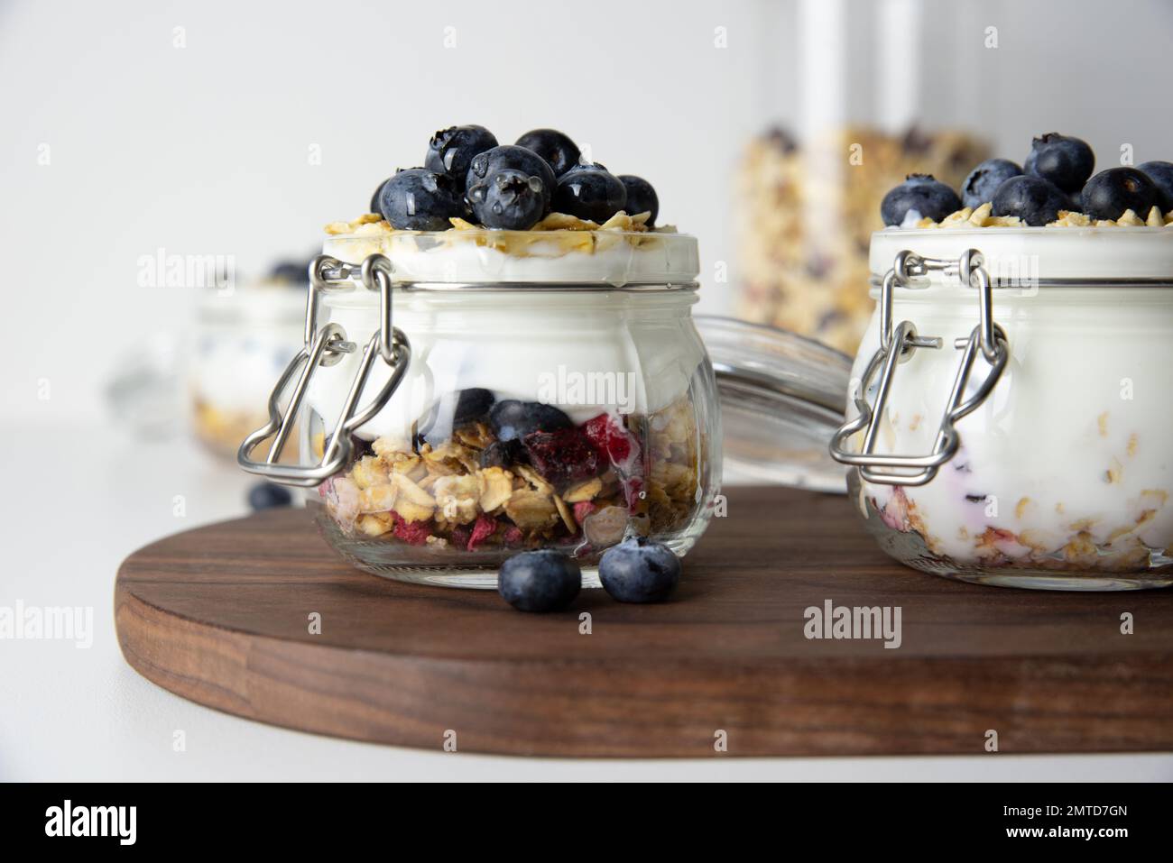 La prima colazione avene con frutta in un bicchiere di yogurt greco e muesli ricoperti di mirtilli freschi su sfondo bianco Foto Stock