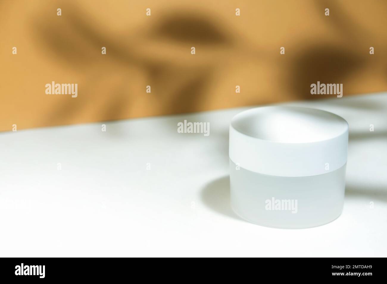 Contenitore bianco vuoto del vaso cosmetico su un fondo bianco beige nei raggi del sole, con le ombre dure dal raheniya. Cosmetologia o cura della pelle Foto Stock