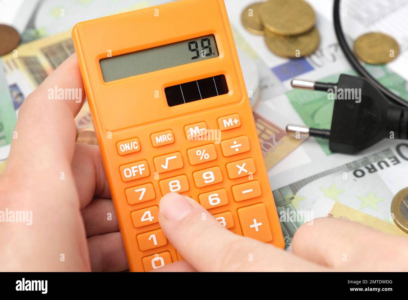 Persona che conta e calcola il costo denaro di elettricità e bolletta di riscaldamento. Cappellino elettrico, lampadina e banconote in euro sullo sfondo. Aumento in t Foto Stock