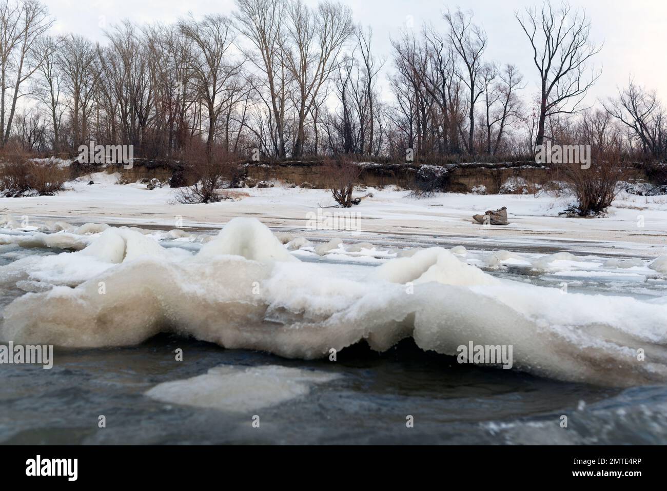 Il primo ghiaccio debole sorge in onde dal flusso d'acqua vicino alla riva. Foto Stock