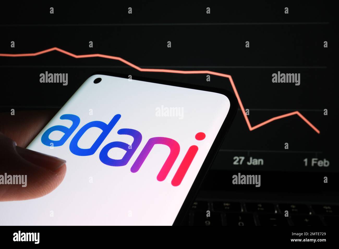 Logo del gruppo Adani visualizzato sullo schermo dello smartphone e grafico del calo dei prezzi delle azioni dell'azienda visualizzato sullo sfondo sfocato. Grafico delle scorte reali per un mese Foto Stock