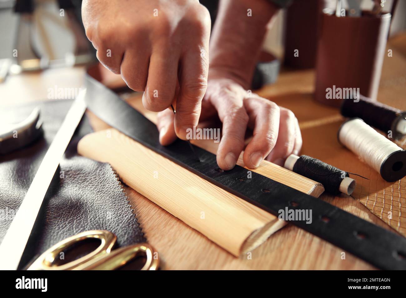 Uomo che fa buchi nella cintura di pelle con cucitura a punteruolo in  officina Foto stock - Alamy