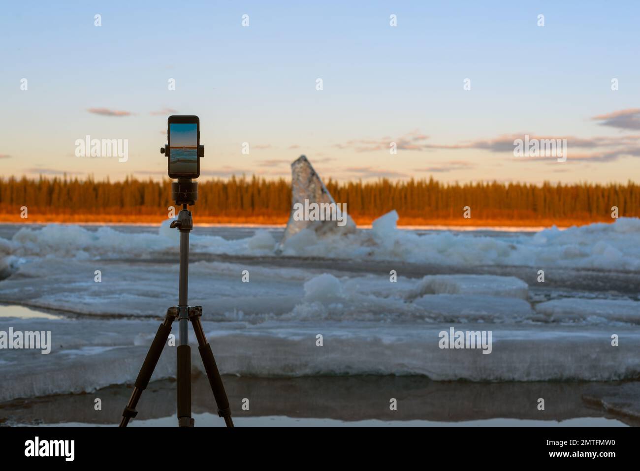 Un telefono cellulare scatta una foto della deriva del ghiaccio primaverile mentre si trova su un cavalletto con un meccanismo rotante per scattare foto panoramiche, sullo sfondo Foto Stock