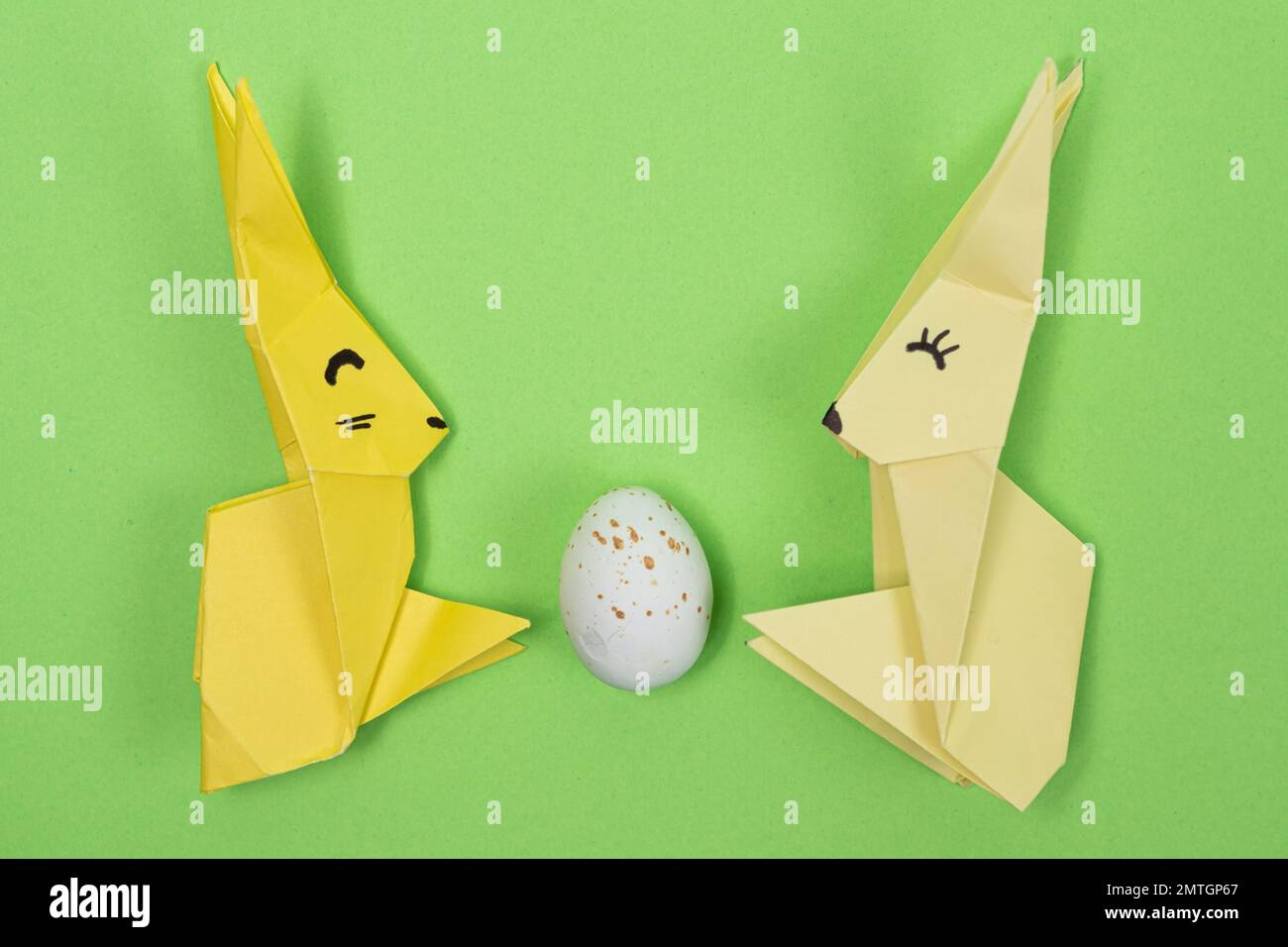 Origami di Pasqua - due coniglietti di carta e un uovo, sfondo verde. Artigianato per le vacanze, fatelo da soli. Foto Stock