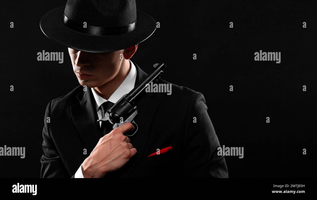 Elegante ritratto di gangster del 1940s con una pistola. Uomo in tuta nera e cappello con una pistola su sfondo scuro. Foto Stock