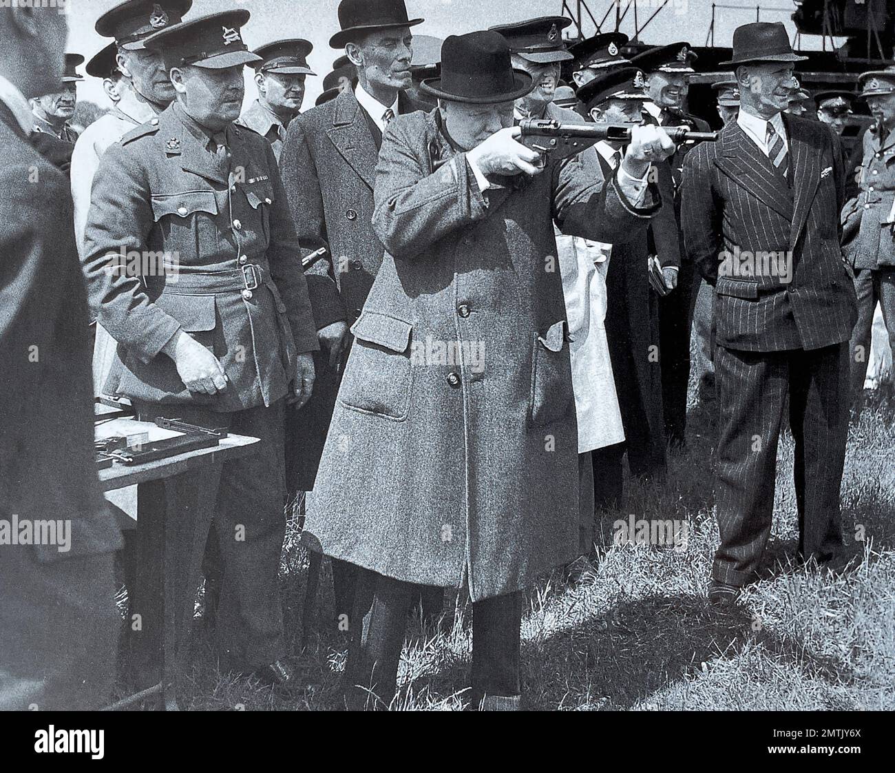 WINSTON CHURCHILL (1874-1955) il 13 giugno 1941 fir9ng una nuova pistola Sten sorvegliata da David Margesson, Segretario di Stato per la prima guerra (in cappello da bowler) e dal suo ispettore della guardia del corpo Walter Thompson a destra Foto Stock