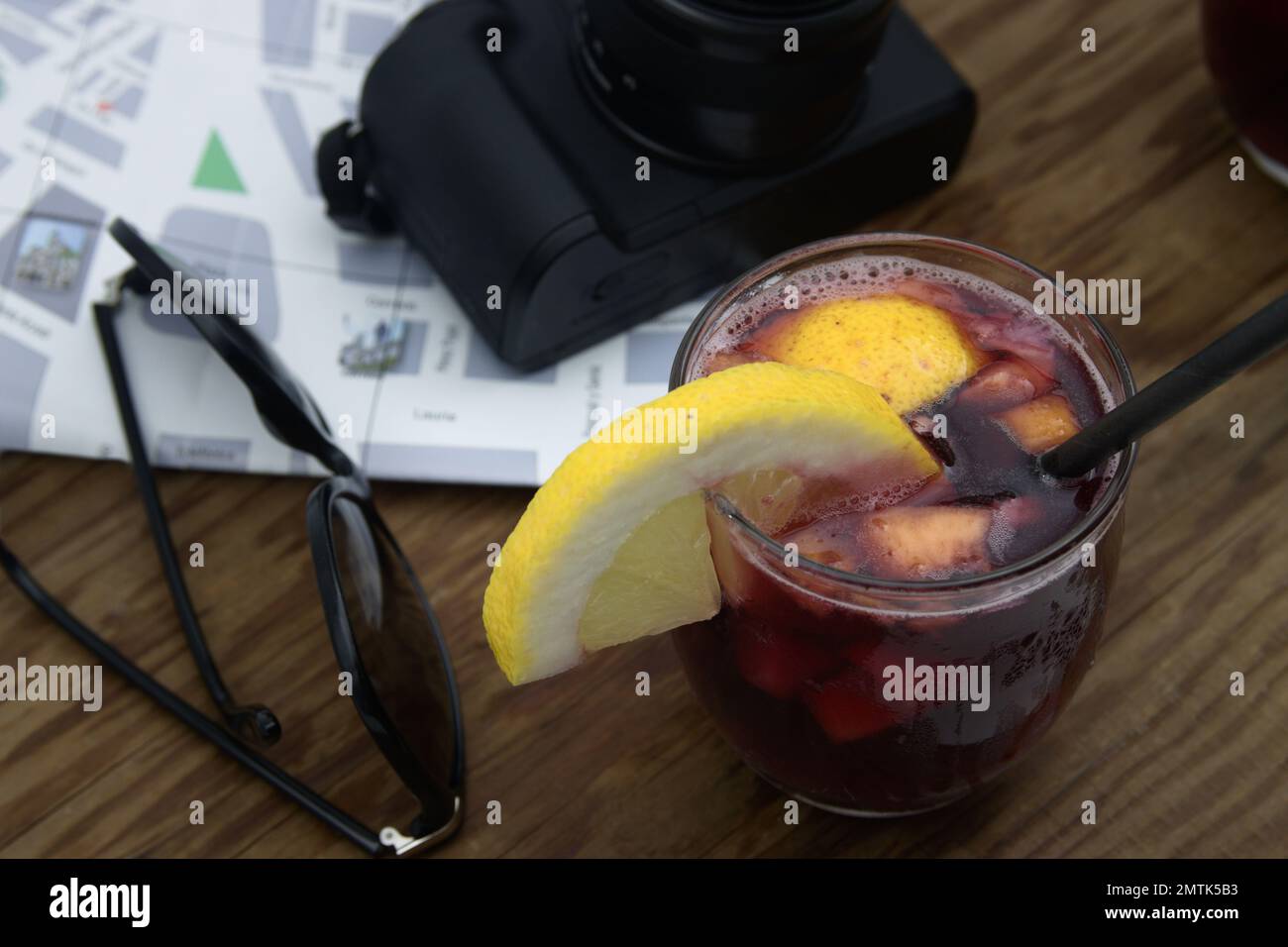 Vista dall'alto di un tavolo dove un turista sta avendo un bicchiere di sangria con limone, accanto a una mappa e una macchina fotografica Foto Stock