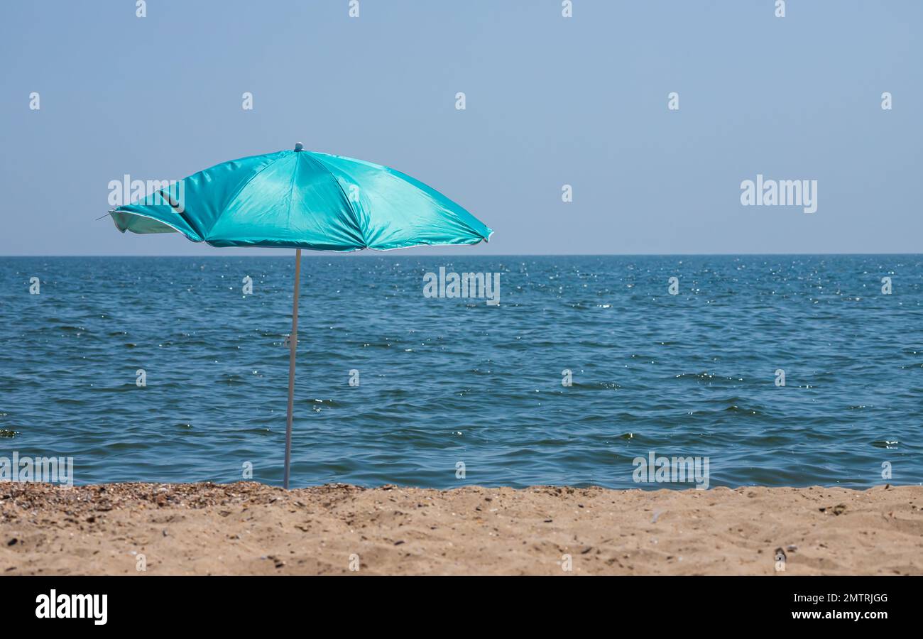 Ombrello da spiaggia con strisce rosa pallido in primo piano, sullo sfondo blu del mare. Foto Stock