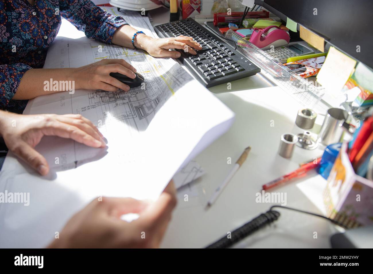 Mani di due colleghi al lavoro in un ufficio tecnico, lavorando sul pc ed esaminando un disegno. Foto Stock