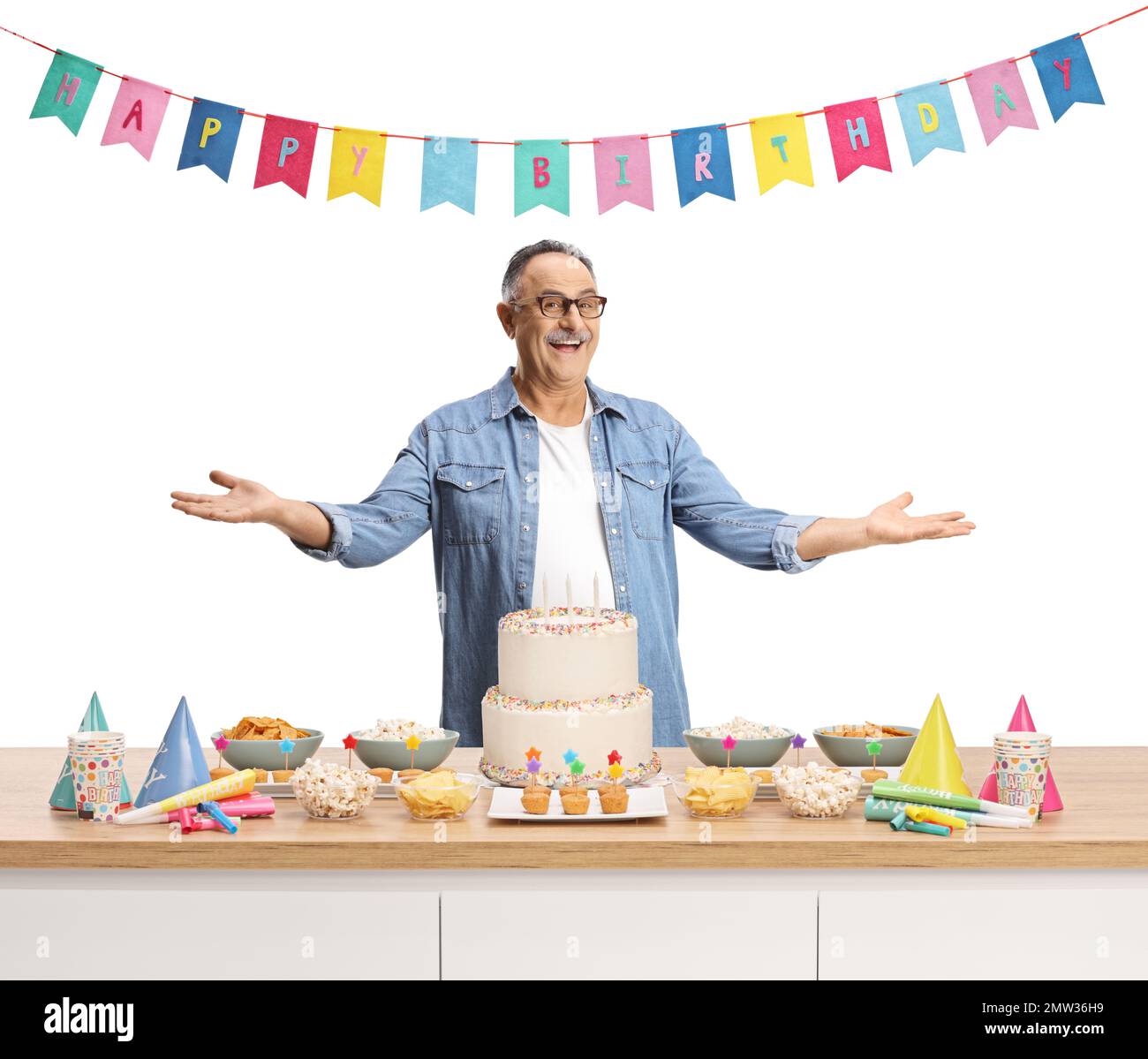 Uomo maturo in piedi dietro un bancone con torta e decorazioni e celebrare il compleanno isolato su sfondo bianco Foto Stock