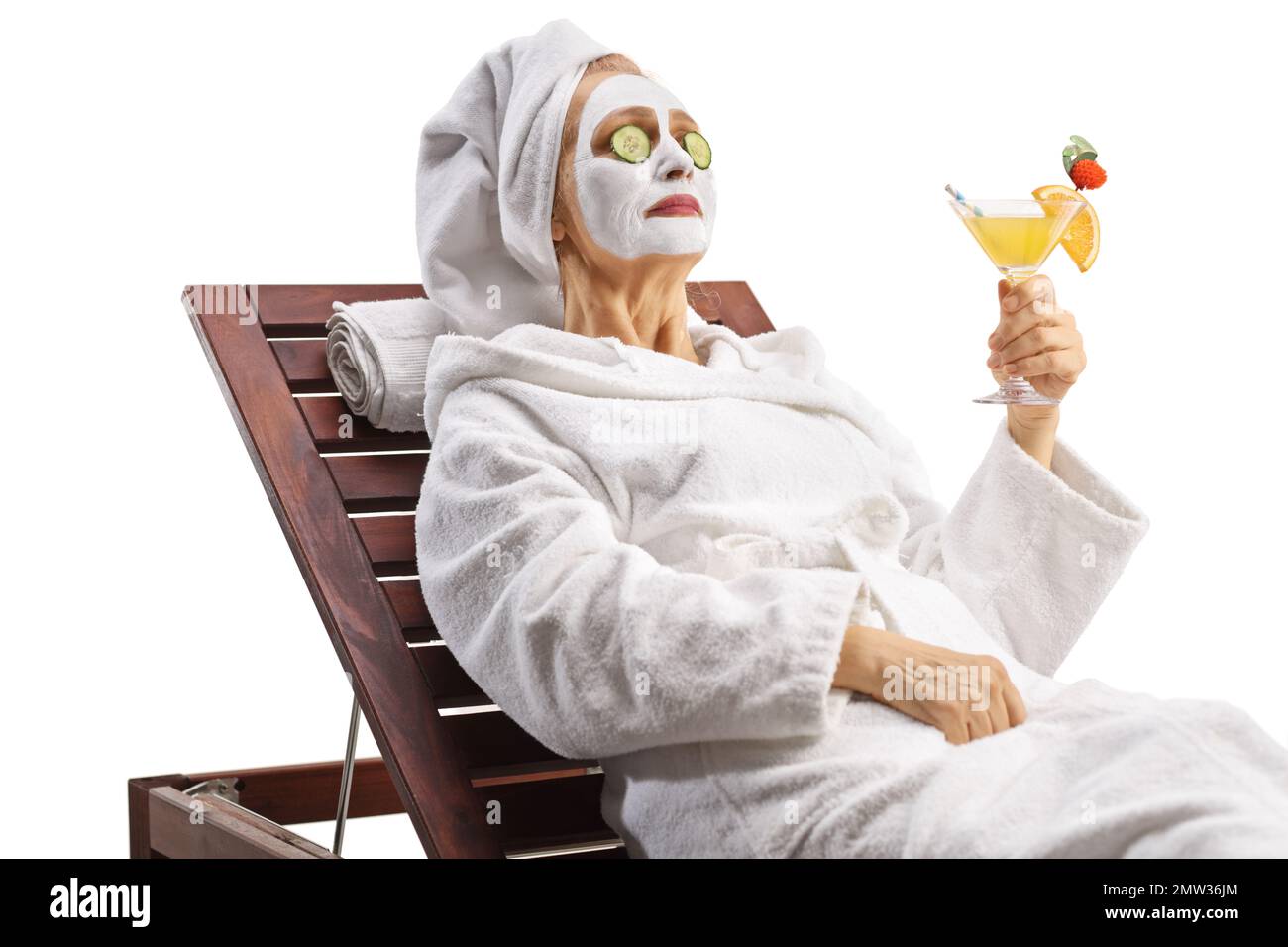 Donna con asciugamano sulla testa e una maschera facciale appoggiata su una poltrona con un cocktail isolato su sfondo bianco Foto Stock