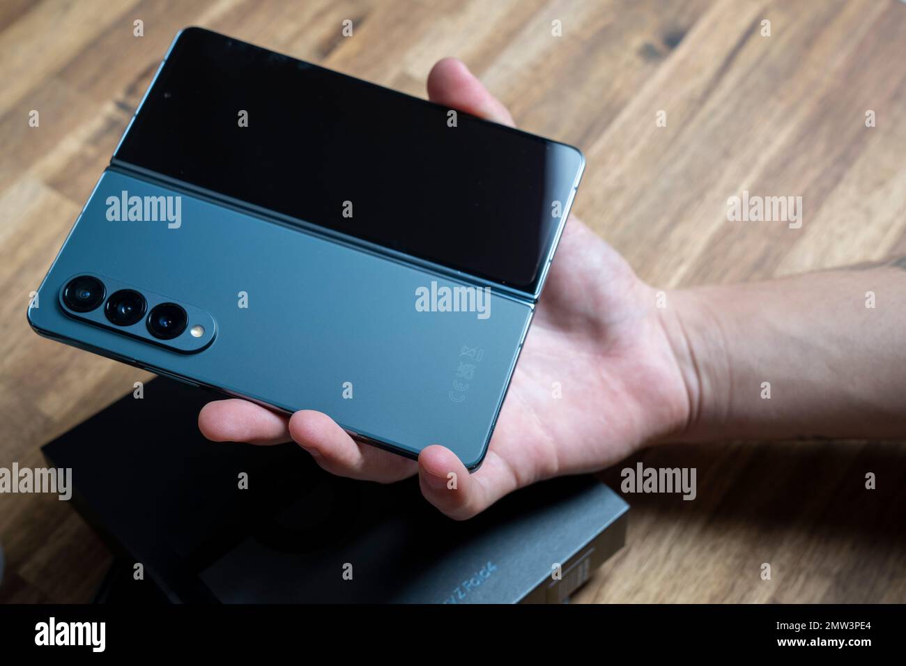 Samsung Galaxy Z Fold 4 in colore grigio-verde. Il dispositivo in posizione aperta nelle mani di un uomo. Un tavolo di legno sullo sfondo. Foto Stock