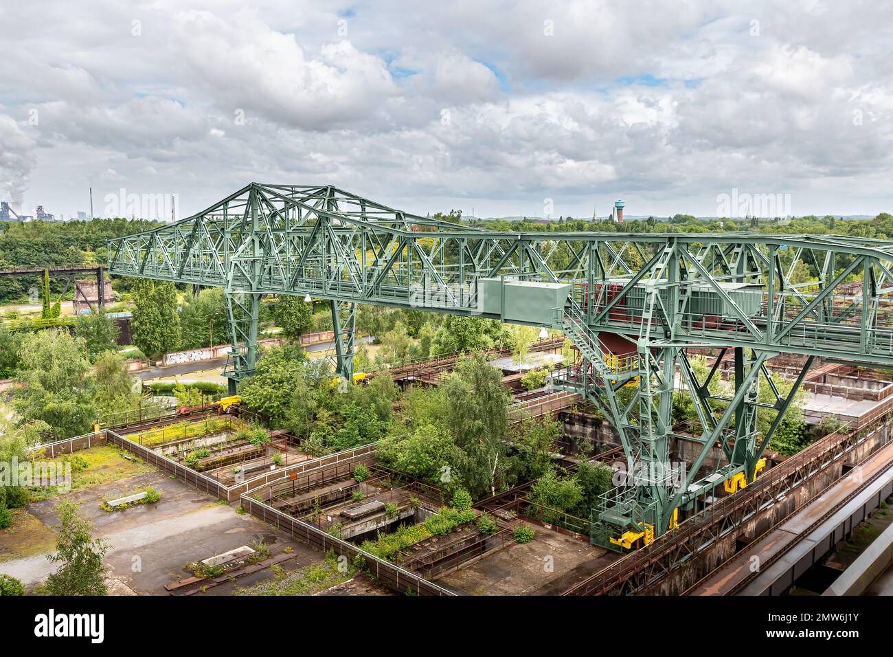 un'enorme installazione di gru in acciaio in un sito di collisione in disuso. I vecchi bacini di carbone sono già coperti da piante verdi Foto Stock