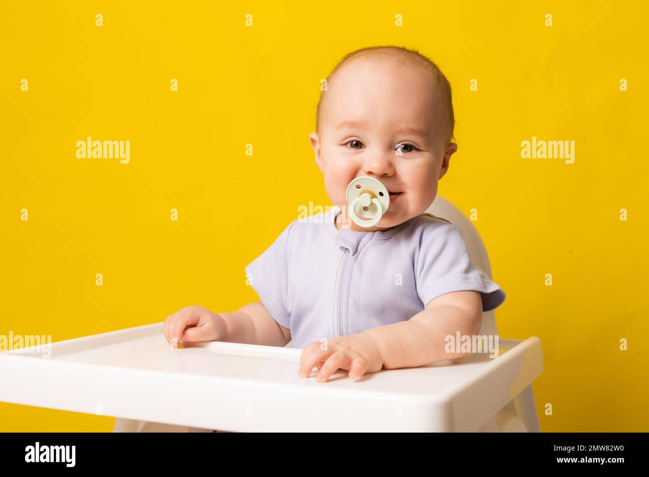 bambino carino con un succhietto in bocca in un seggiolone su uno sfondo giallo. Pappe per bambini, spazio per il testo. Foto di alta qualità Foto Stock