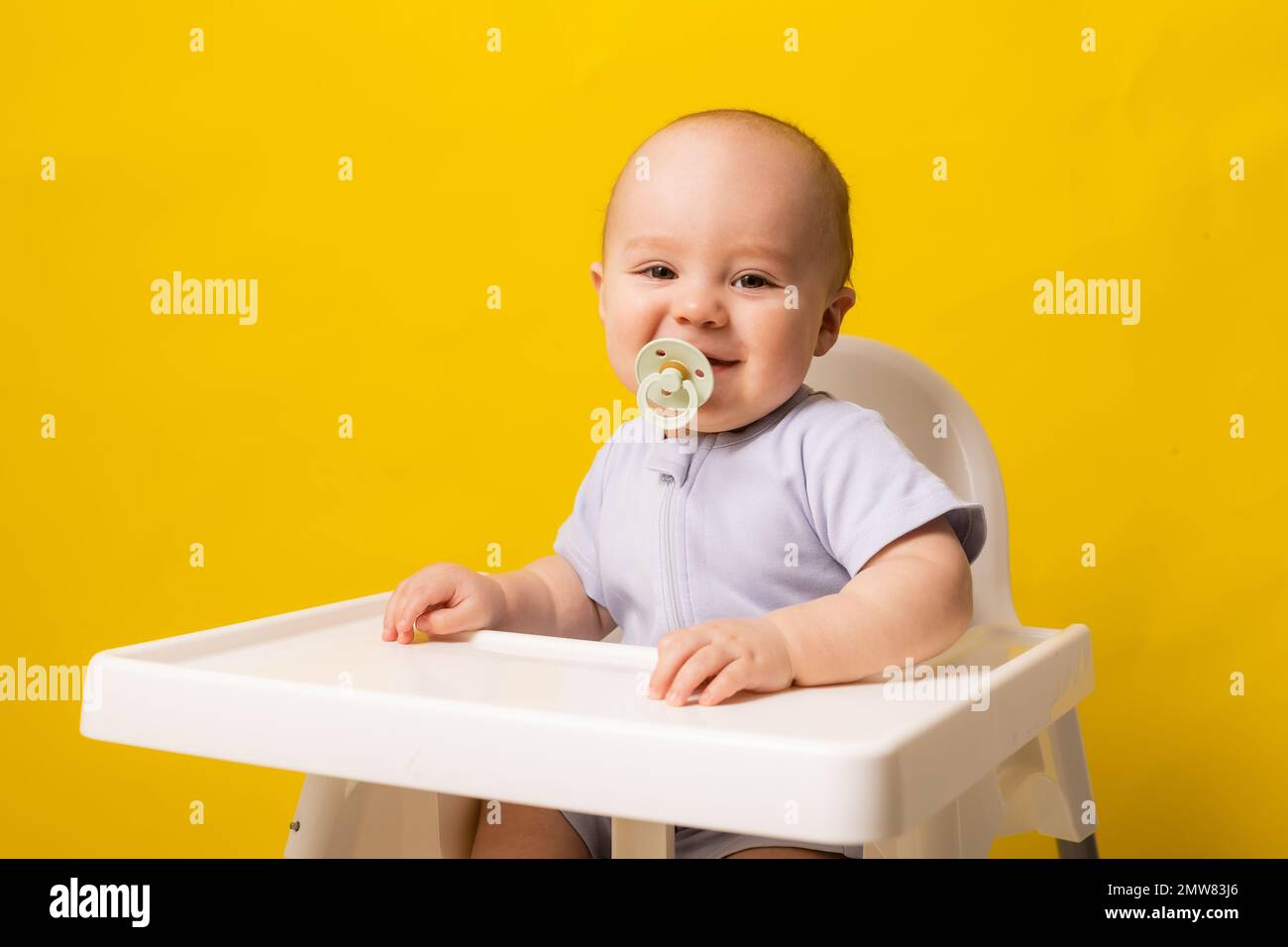 bambino carino con un succhietto in bocca in un seggiolone su uno sfondo giallo. Pappe per bambini, spazio per il testo. Foto di alta qualità Foto Stock