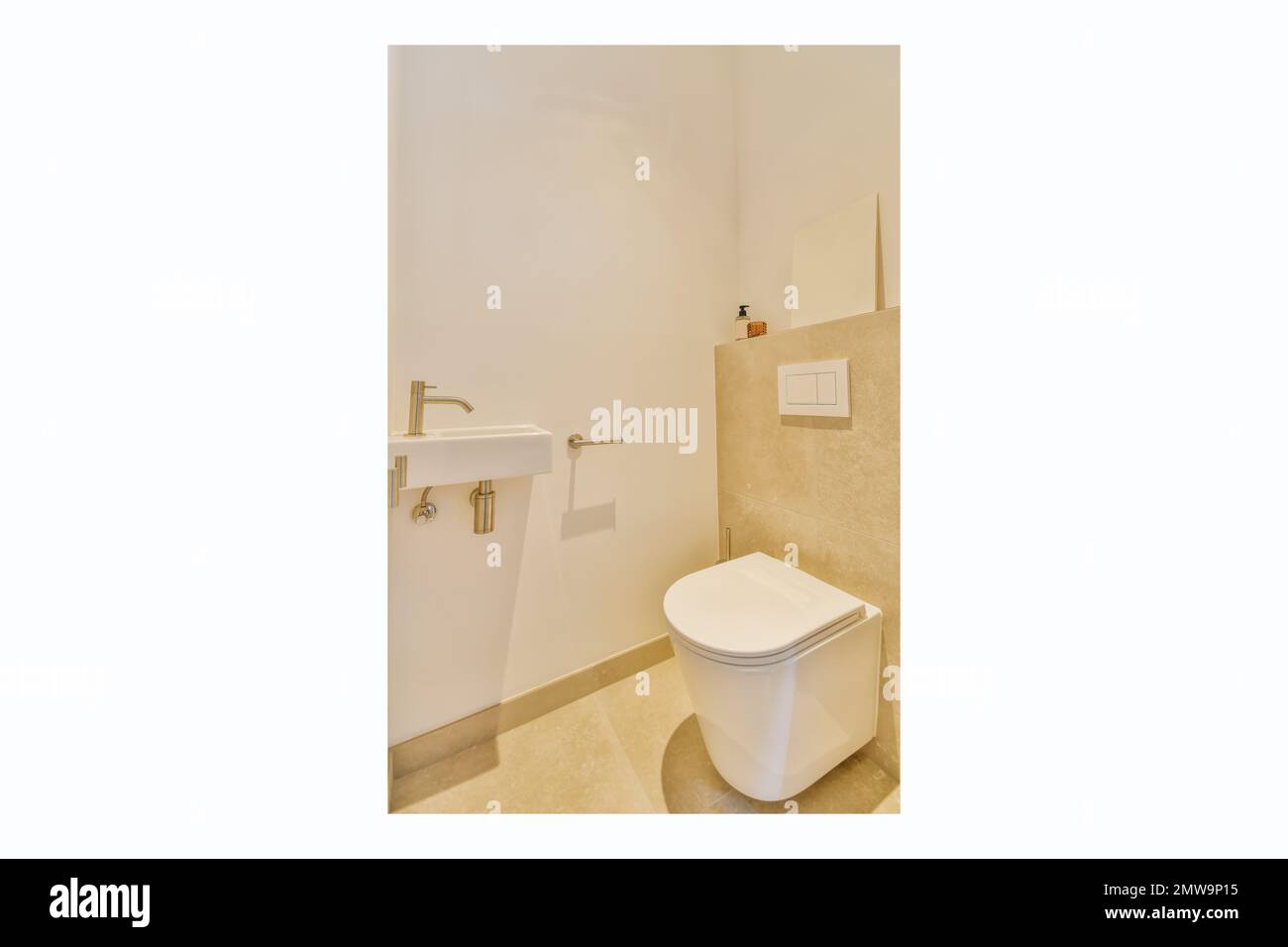 una toilette bianca e un lavandino in un bagno con piastrelle beige sulla parete dietro e' un pavimento piastrellato marrone chiaro Foto Stock