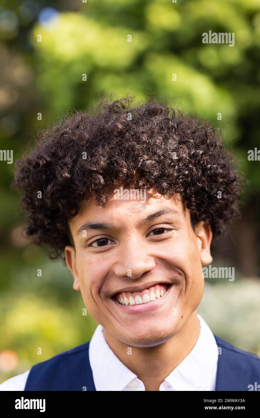 Ritratto verticale dello sposo biraciale sorridente con capelli ricci in giardino al matrimonio all'aperto Foto Stock