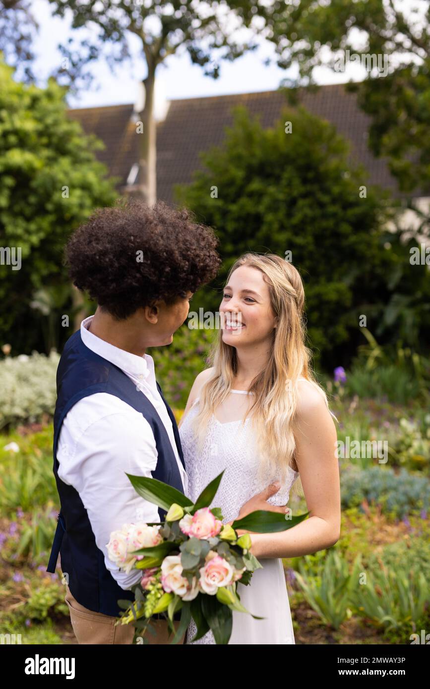 Verticale di spose diverse felice e sposo che tiene bouquet e sorridente al matrimonio all'aperto Foto Stock