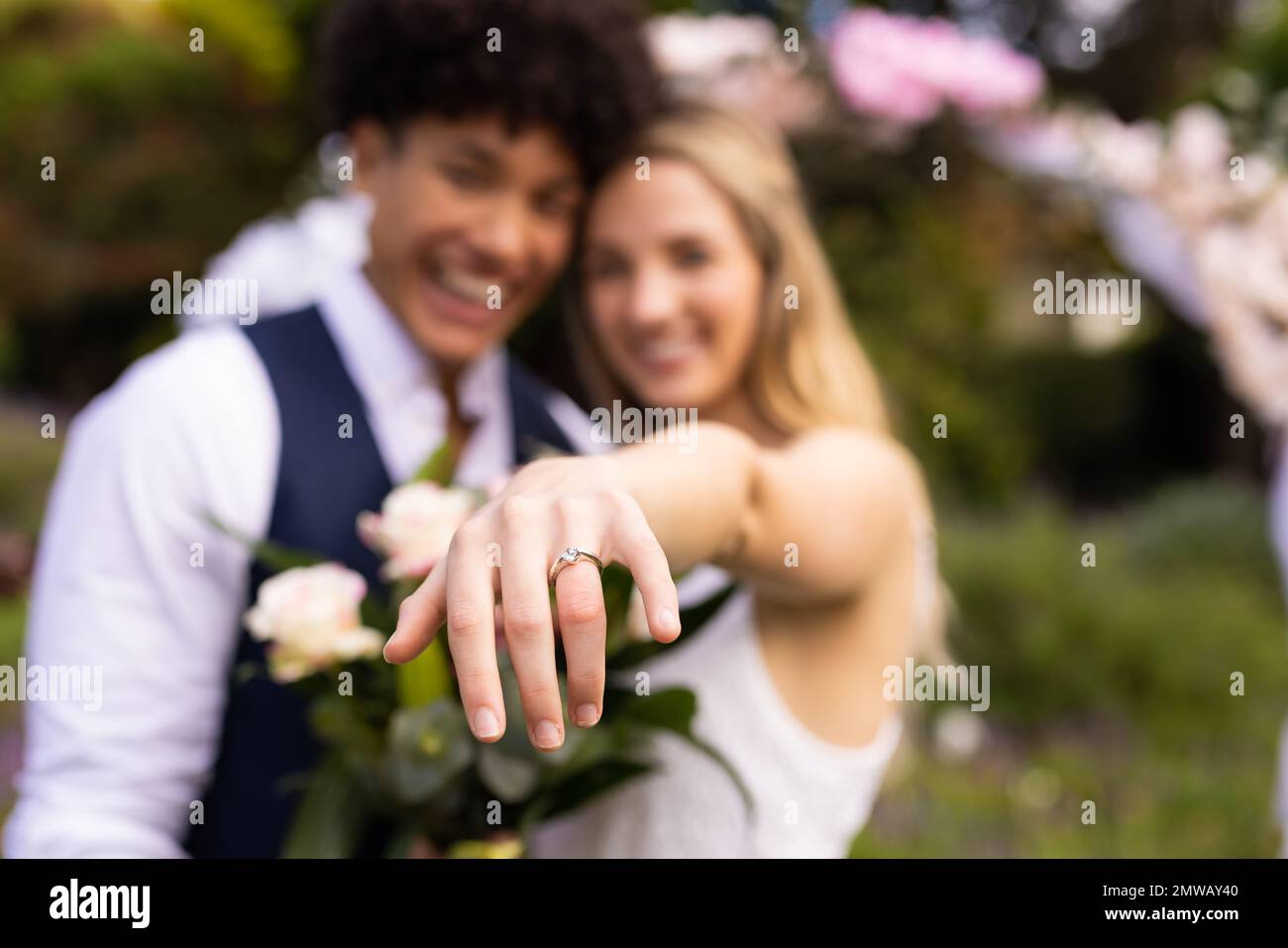 Sposi e sposi variegati felici, sposi che mostrano l'anello alla macchina fotografica alle nozze esterne, fuoco selettivo Foto Stock