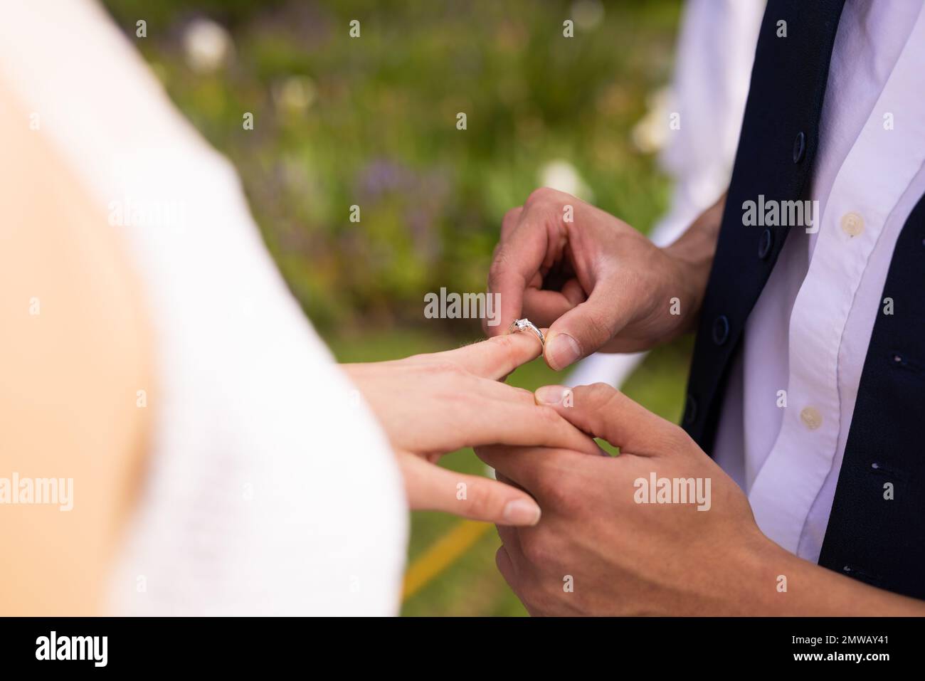 A metà dello sposo diverso che mette l'anello sul dito della sposa alle nozze esterne, spazio della copia Foto Stock