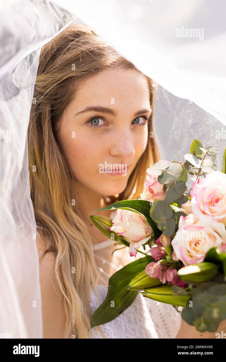 Ritratto verticale della sposa caucasica in velo bianco con bouquet in occasione di un matrimonio all'aperto Foto Stock