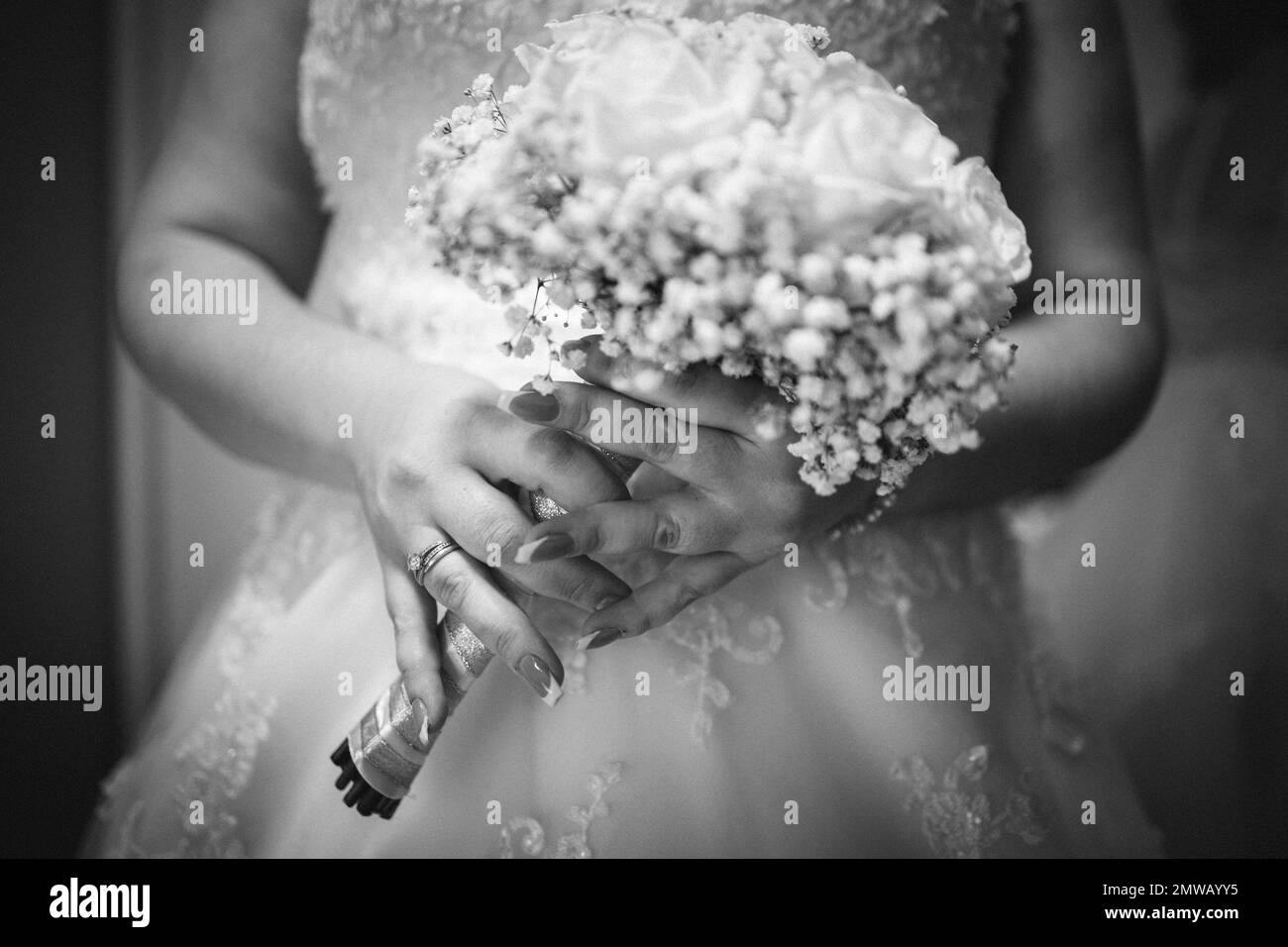 Un primo piano di una sposa che tiene un bouquet di fiori in scala di grigi Foto Stock