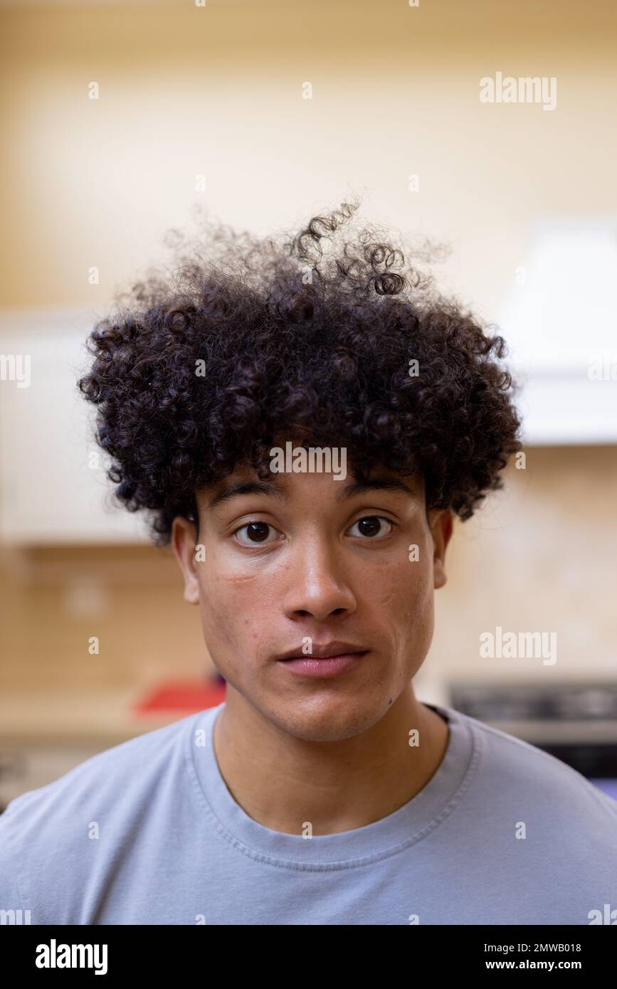 Ritratto verticale dell'uomo biraciale con capelli ricci in cucina a casa Foto Stock