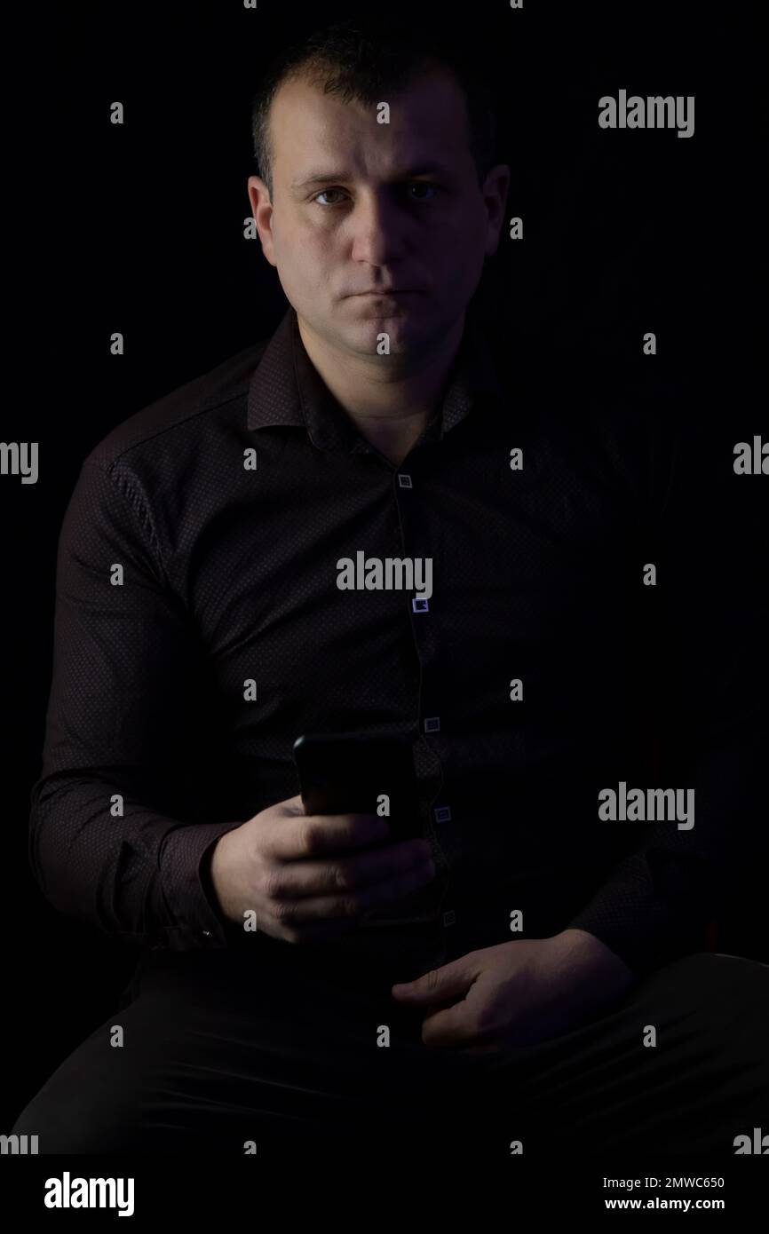 Un uomo con un telefono in una camicia su uno sfondo nero. Foto Stock