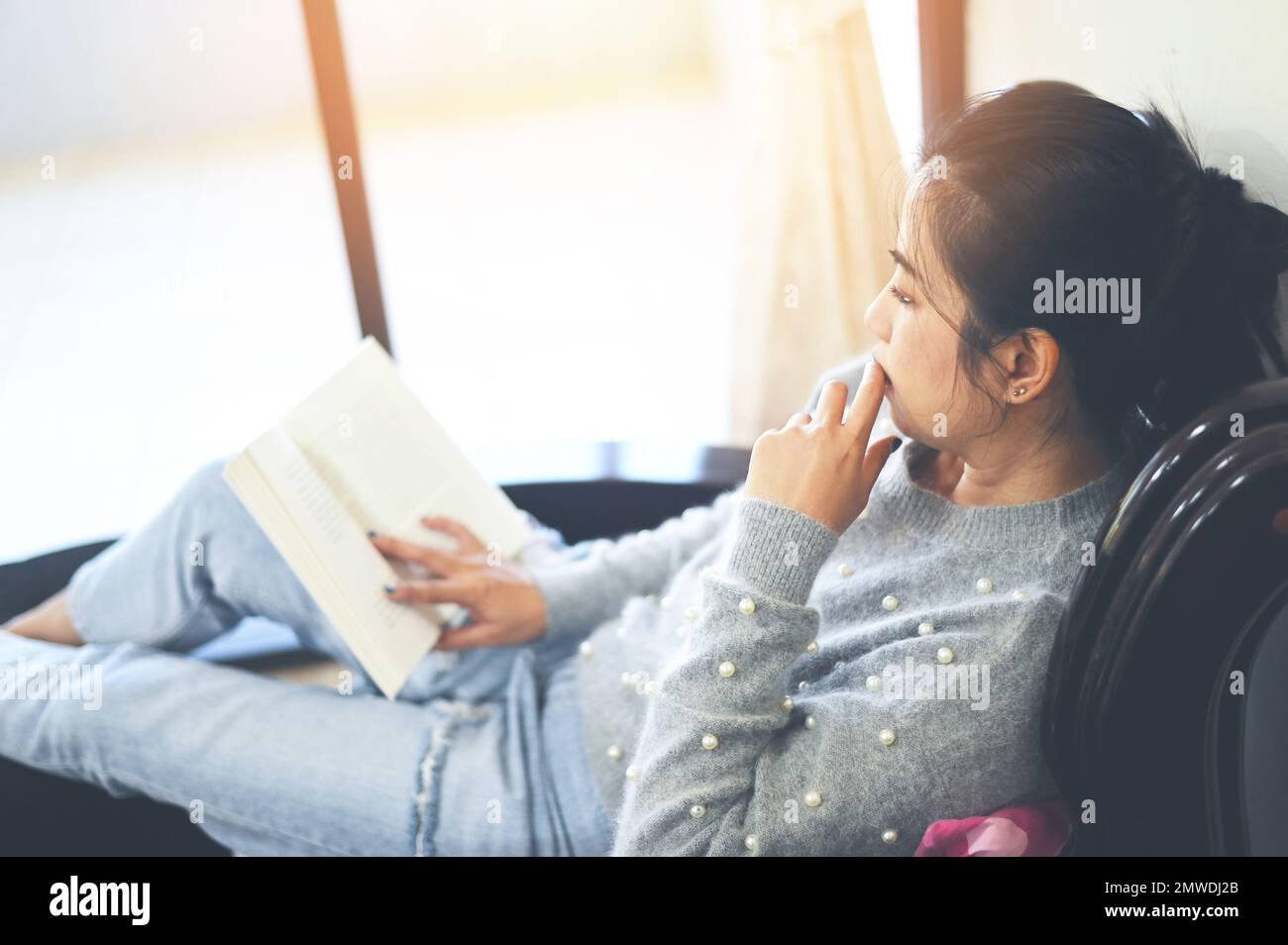 donna che si rilassa a casa, donna lettura libro deporre su divano di legno - rilassarsi nel suo soggiorno leggere libro in vacanza è preferito hobby in casa an Foto Stock