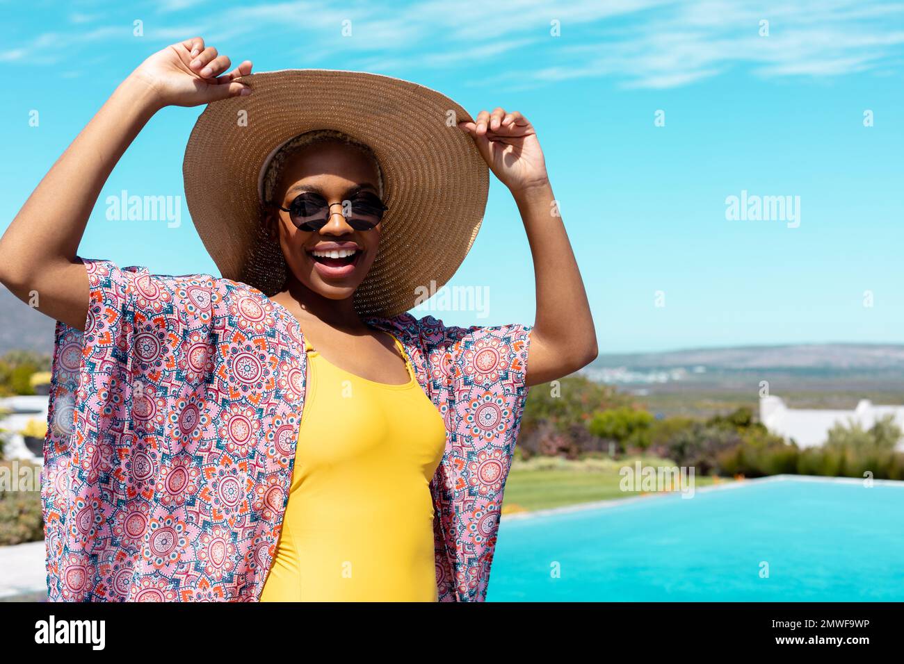 Ritratto di felice ragazza afro-americana che indossa cappello di paglia e occhiali da sole in piscina Foto Stock